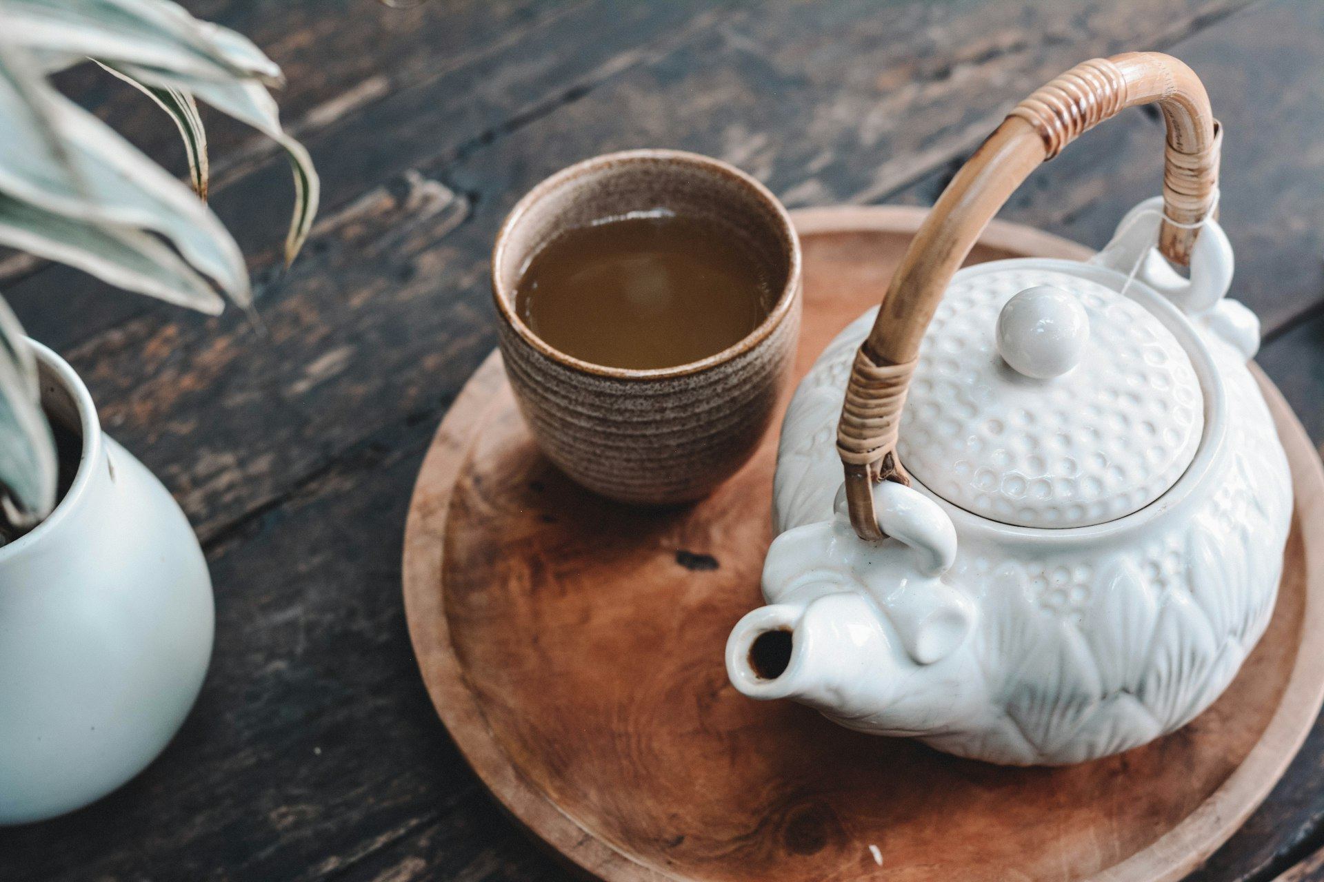 Herbal tea in a ceramic cup beside a white teapot