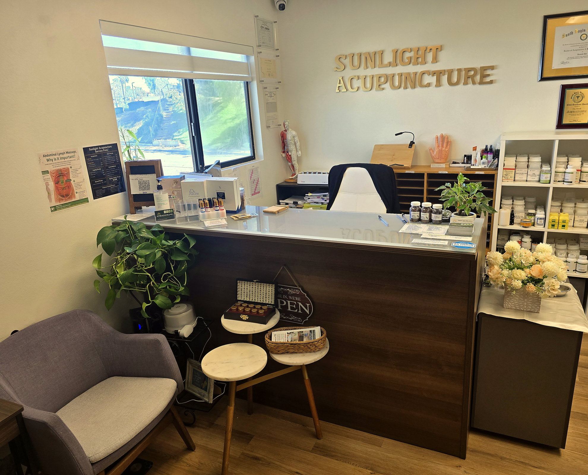 Reception desk at Sunlight Acupuncture in Brea, with the clinic name on the wall, herbal shelves, and daylight from the front window